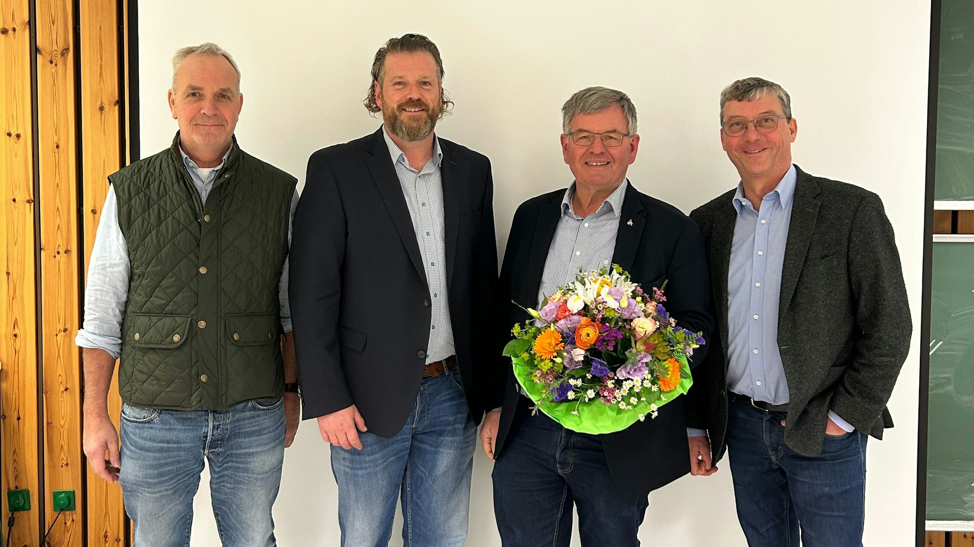 Vier Männer lächeln, einer hält einen Blumenstrauß.