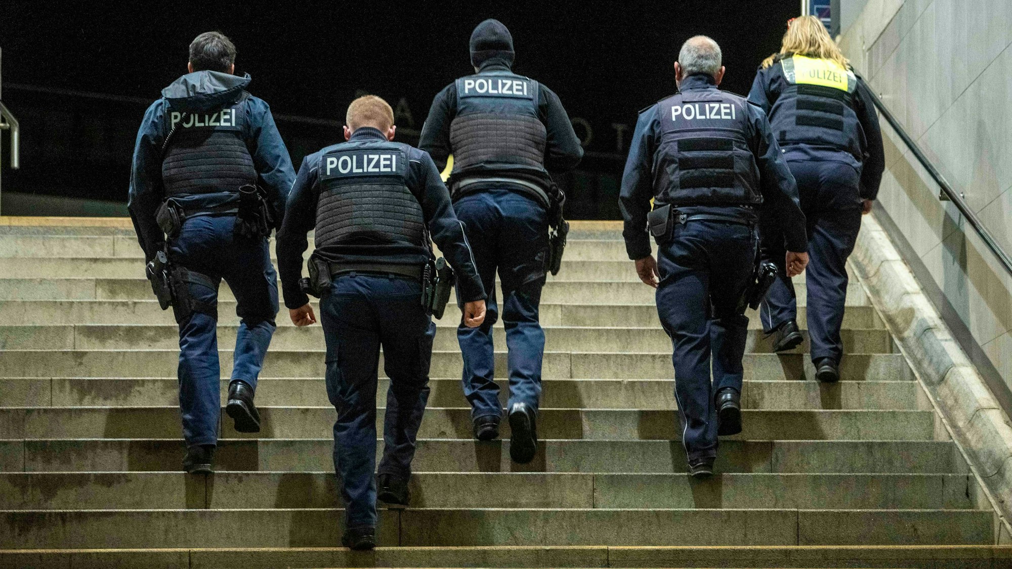 Fünf Menschen mit der Aufschrift „Polizei“ auf ihren Westen gehen eine Treppe hoch.
