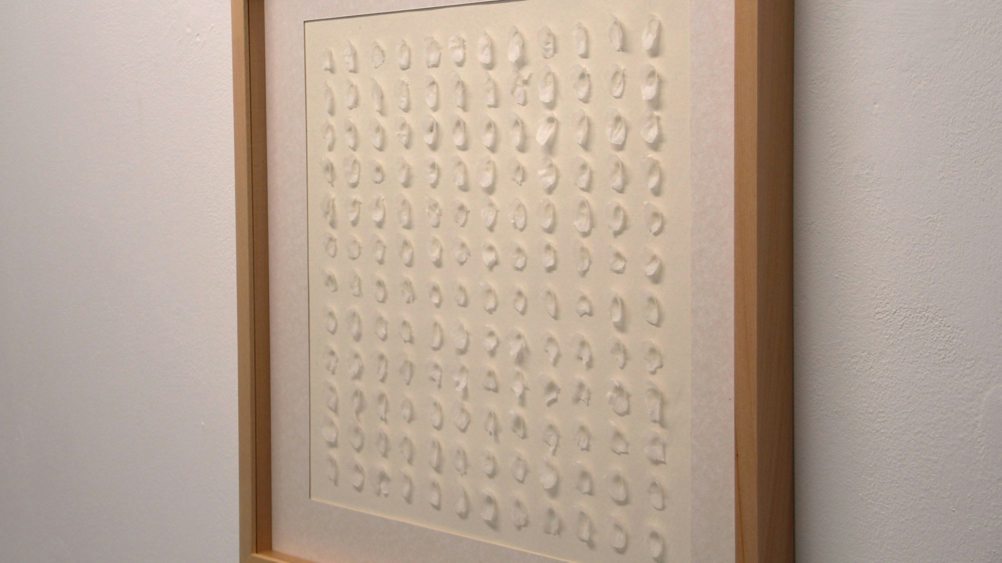 Ein Bild mit weißen Wachsflecken auf weißem Grund hängt an einer Wand.