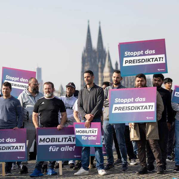 Teilnehmer einer Demonstration halten Schilder mit der Aufschrift „Stoppt das Preisdiktat“ in den Händen. Die Kundgebung richtet sich gegen Pläne der Stadt Köln zur Einführung von Mindestpreisen bei Unternehmen wie Uber und Bolt.