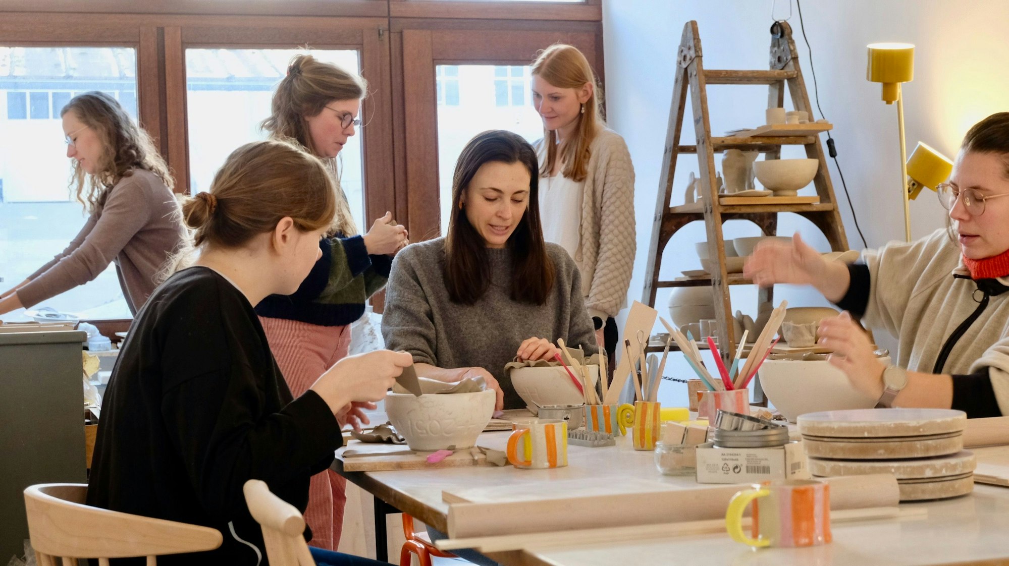 Frauen sind ein einem Atelier, einige sitzen andere stehen, gearbeitet wird meist an Schüsseln aus Ton.