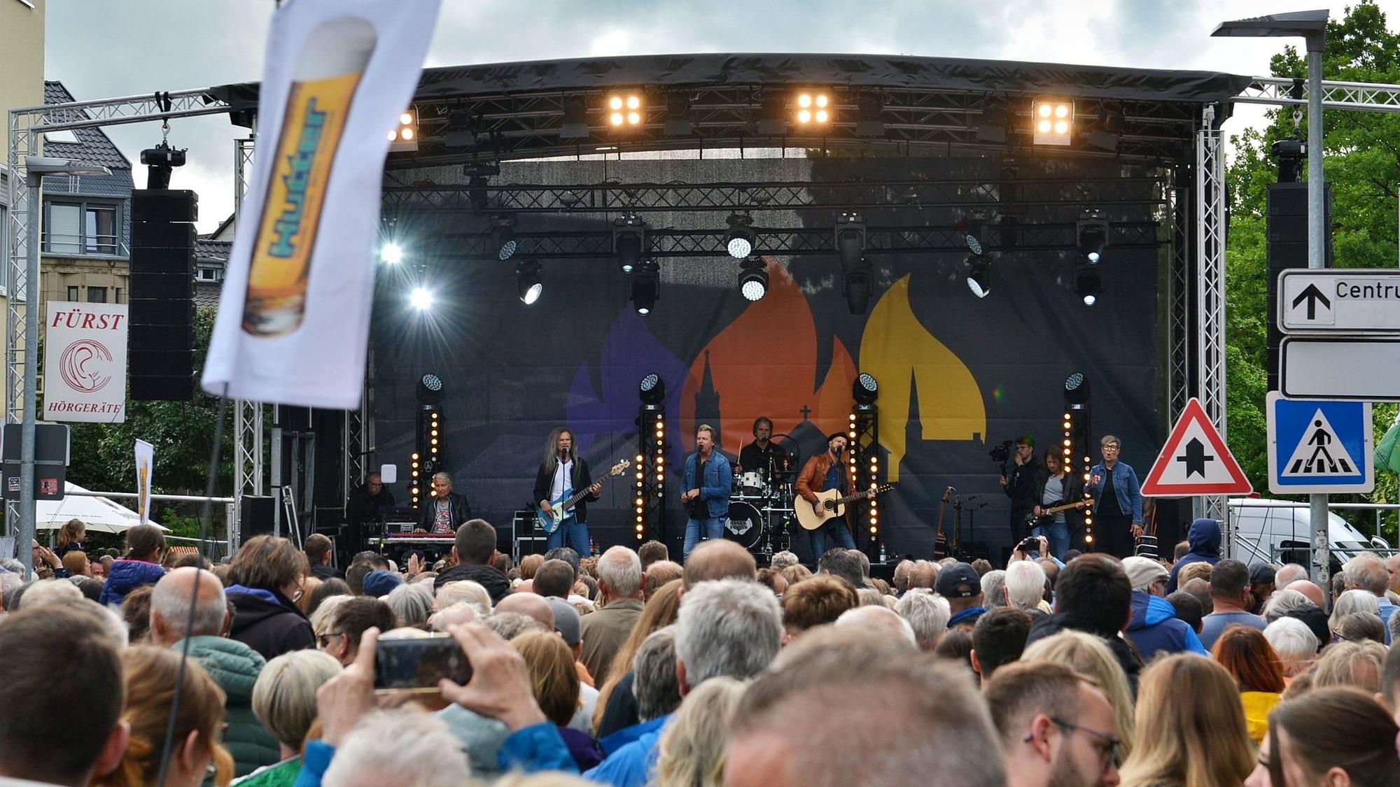 Auf einer überdachten Bühne spielt eine Musikgruppe vor großem Publikum.