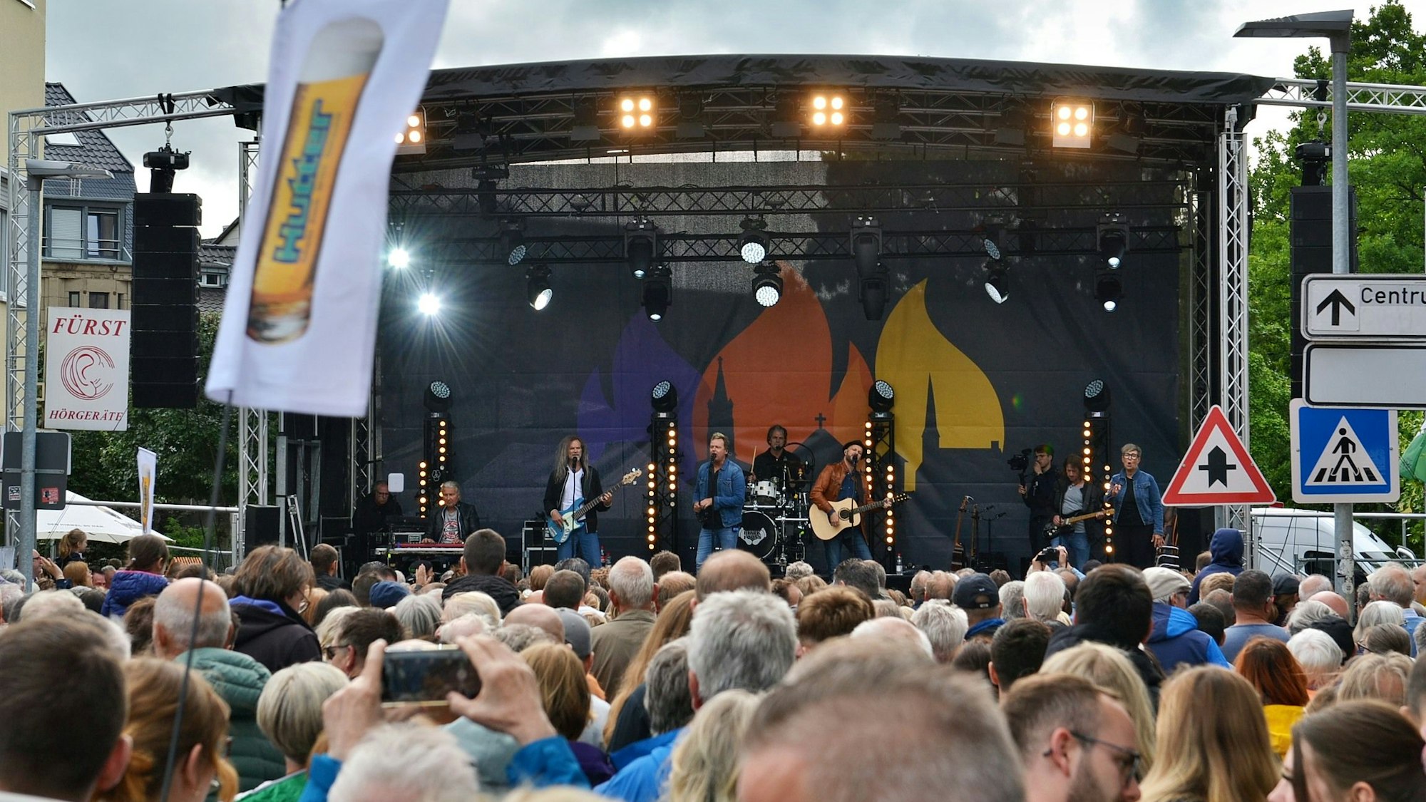 Auf einer überdachten Bühne spielt eine Musikgruppe vor großem Publikum.