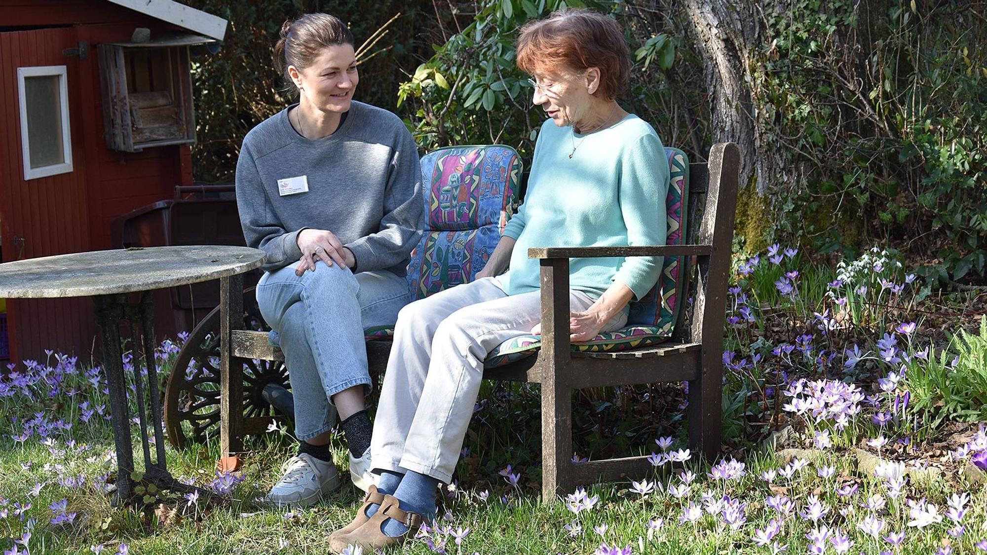Psychoonkologin Julia Ammann und Patientin Anni Hermans-Conrads sitzen auf einer Bank im Grünen.
