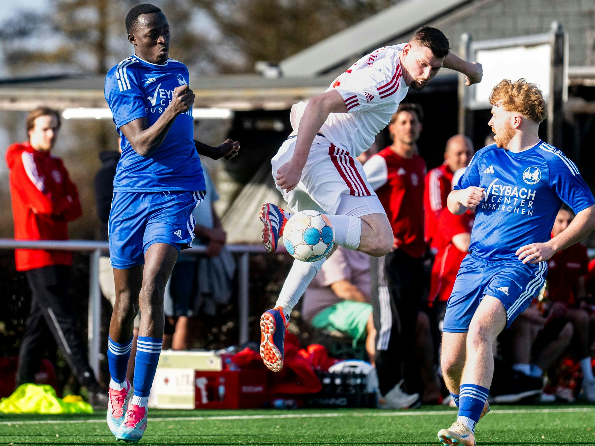 Springend klärt Marcel Heindrichs den Ball gegen zwei Weilerswister Spieler.