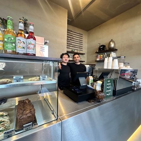 Zwei Männer in schwarzen T-Shirts stehen hinter einem Verkaufstresen.