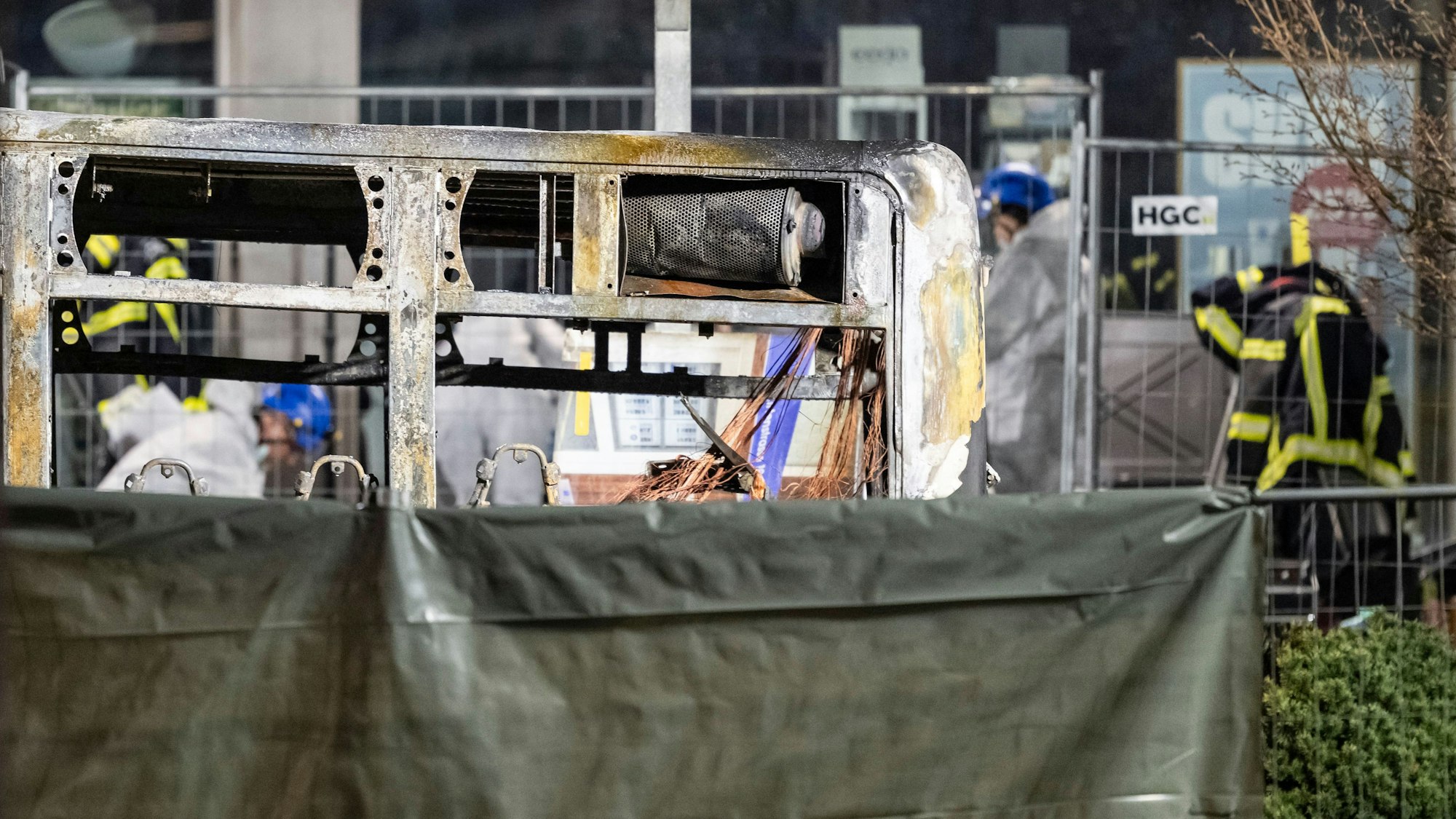 Die verkohlte Hülle eines Linienbusses steht hinter einem Sichtschutz. Es hat Tote und Verletzte gegeben.