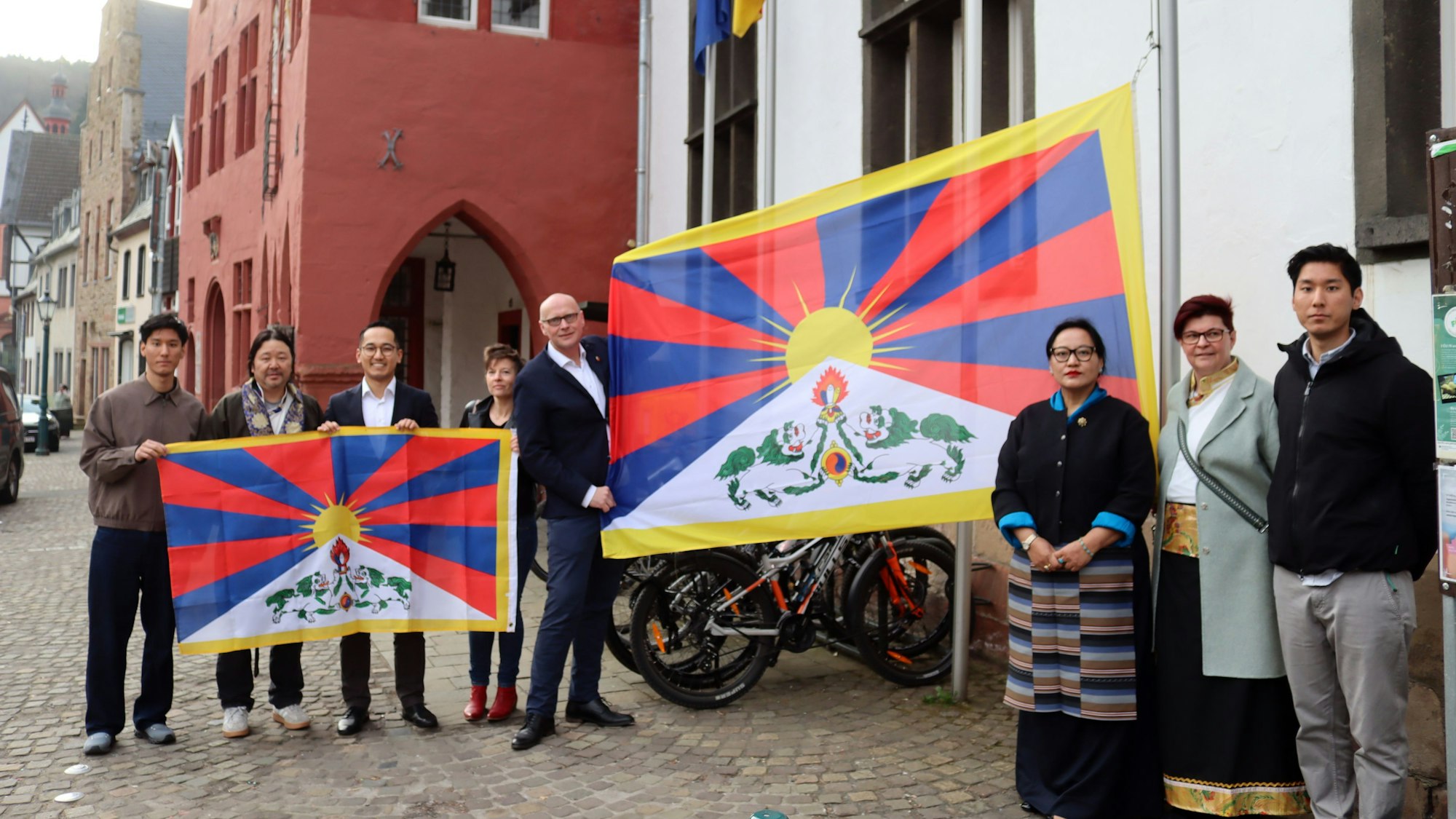 Eine Menschengruppe steht vor dem Bad Münstereifeler Rathaus und hält zwei tibetische Flaggen hoch.