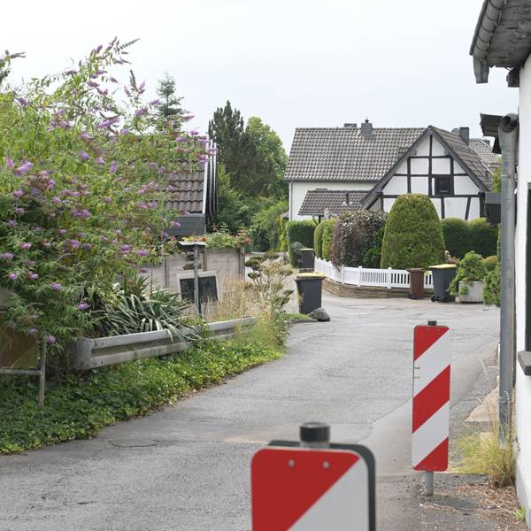 Eine enge Straße mit Linkskurve, rechts Barken und eine Hauswand, links eine Leitplanke