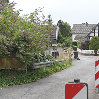 Eine enge Straße mit Linkskurve, rechts Barken und eine Hauswand, links eine Leitplanke