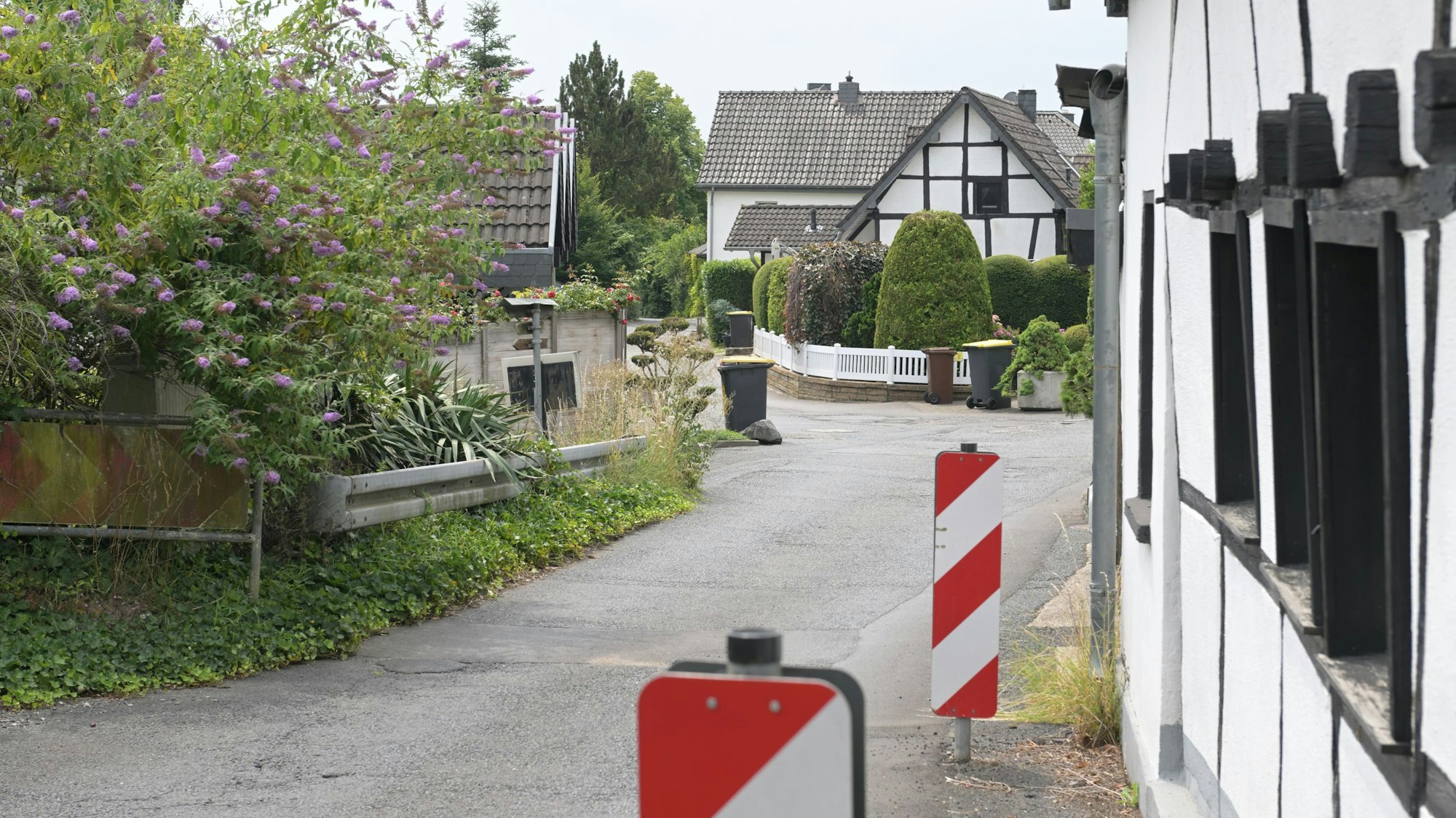 Eine enge Straße mit Linkskurve, rechts Barken und eine Hauswand, links eine Leitplanke