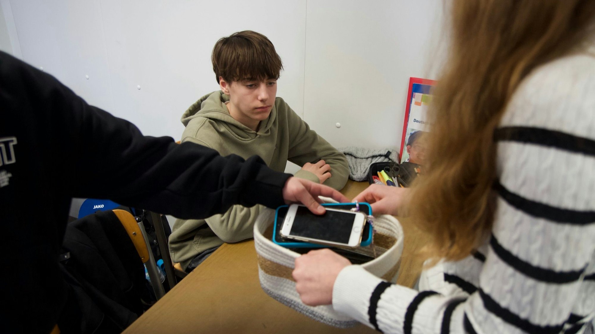 Ein Junge schaut auf den Korb, in den die Jugendlichen ihre Handys legen.