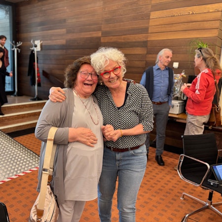 Die Obengenannten stehen nah beieinander, halten sich an einer Hand und strahlen in die Kamera.