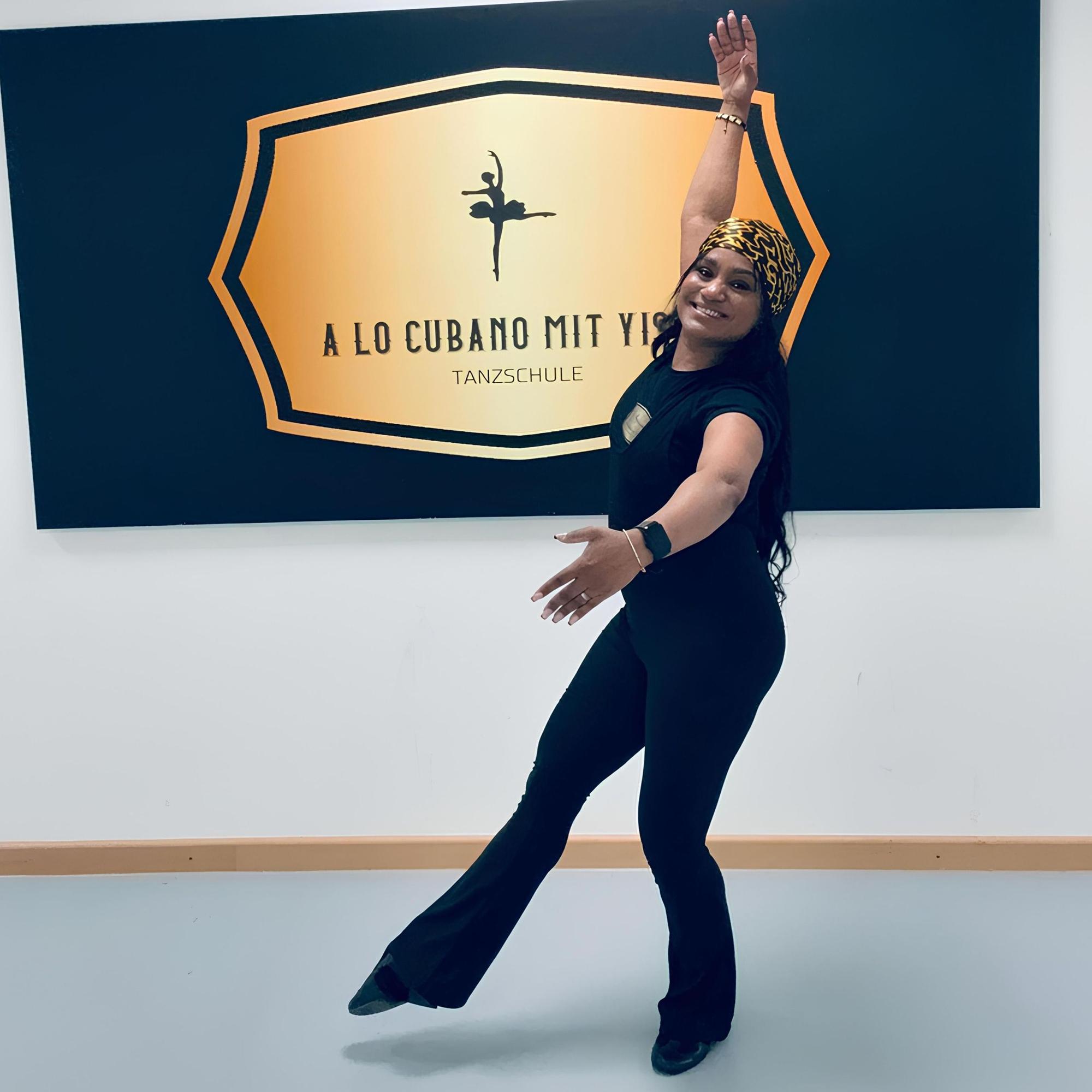 Yiset Bell nimmt vor einem Plakat eine tänzerische Haltung ein. Auf dem Plaket steht „A lo cubano mit Yiset Tanzschule“.
