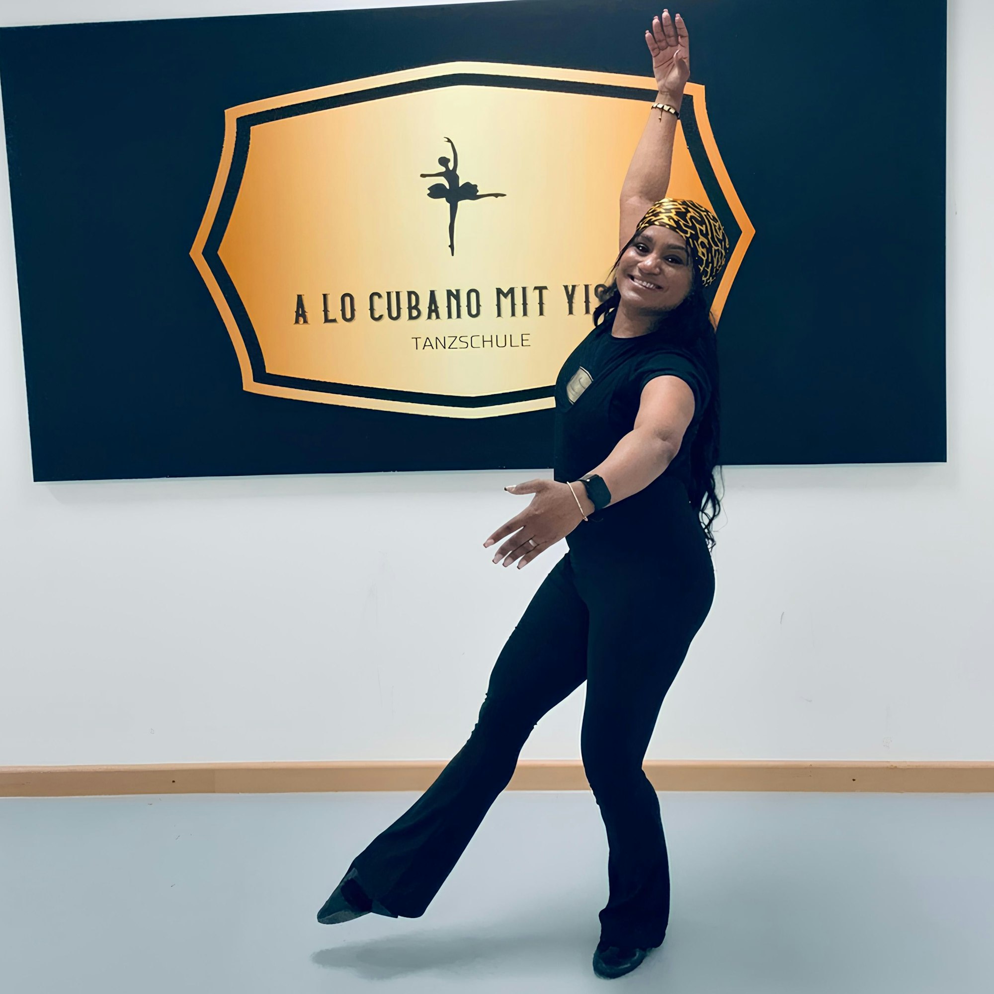 Yiset Bell nimmt vor einem Plakat eine tänzerische Haltung ein. Auf dem Plaket steht „A lo cubano mit Yiset Tanzschule“.