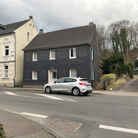 Vor zwei Häusern an der Straße fährt ein Auto vorbei.