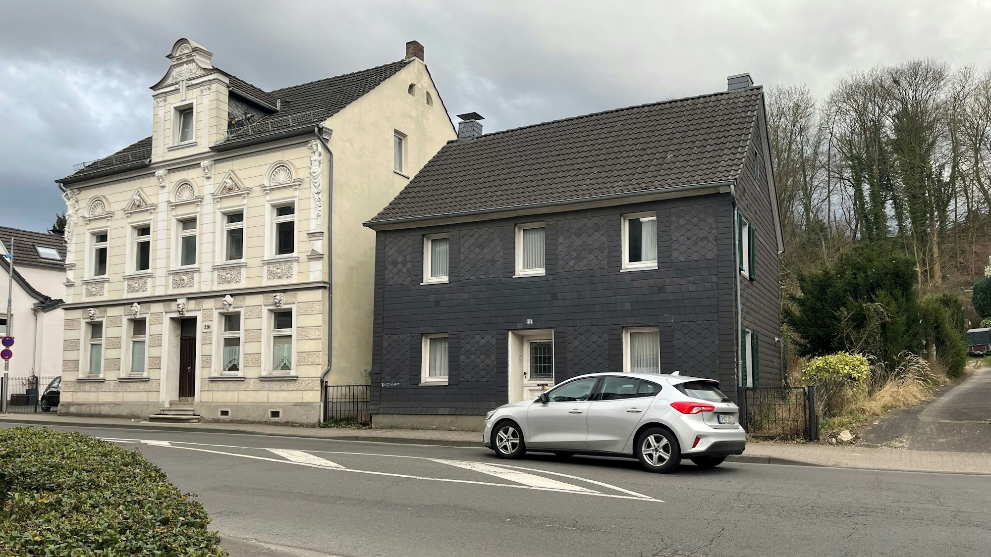 Vor zwei Häusern an der Straße fährt ein Auto vorbei.