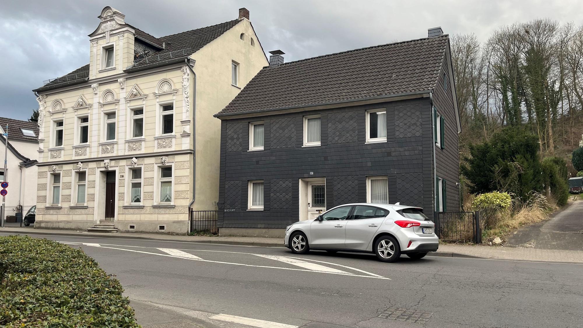 Zwei Häuser stehen nebeneinander. Ein Auto fährt vorbei.