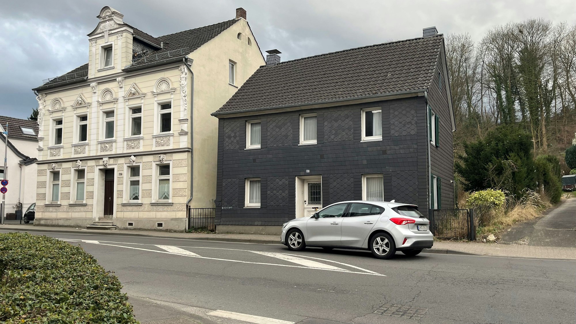 Zwei Häuser stehen nebeneinander. Ein Auto fährt vorbei.