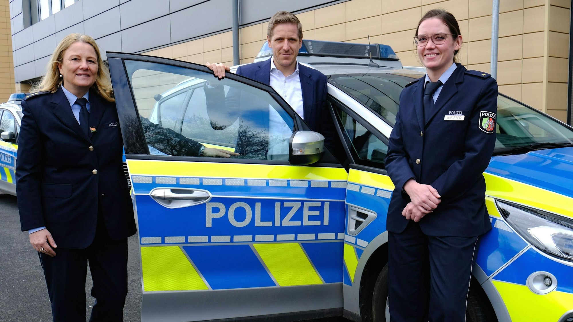 Landrat Markus Ramers (Mitte), Polizeirätin Annika Meister (r.), Direktionsleiterin Verkehr der Kreispolizeibehörde Euskirchen, und Polizeidirektorin Gabriele Mälchers, stehen an einem Streifenwagen.