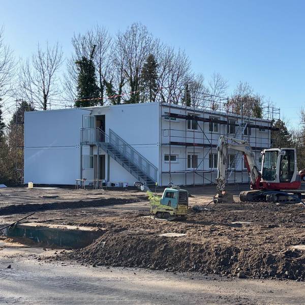 Auf dem Bild ist eine Baustelle mit Modulbauten und einem Bagger zu sehen.