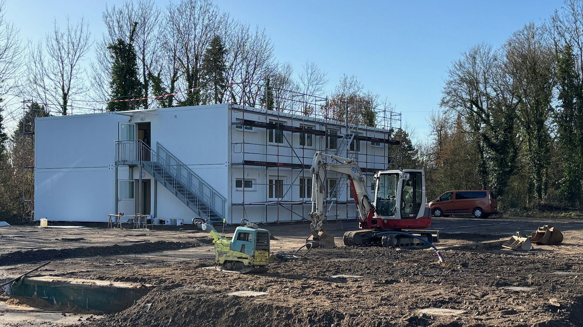 Auf dem Bild ist eine Baustelle mit Modulbauten und einem Bagger zu sehen.