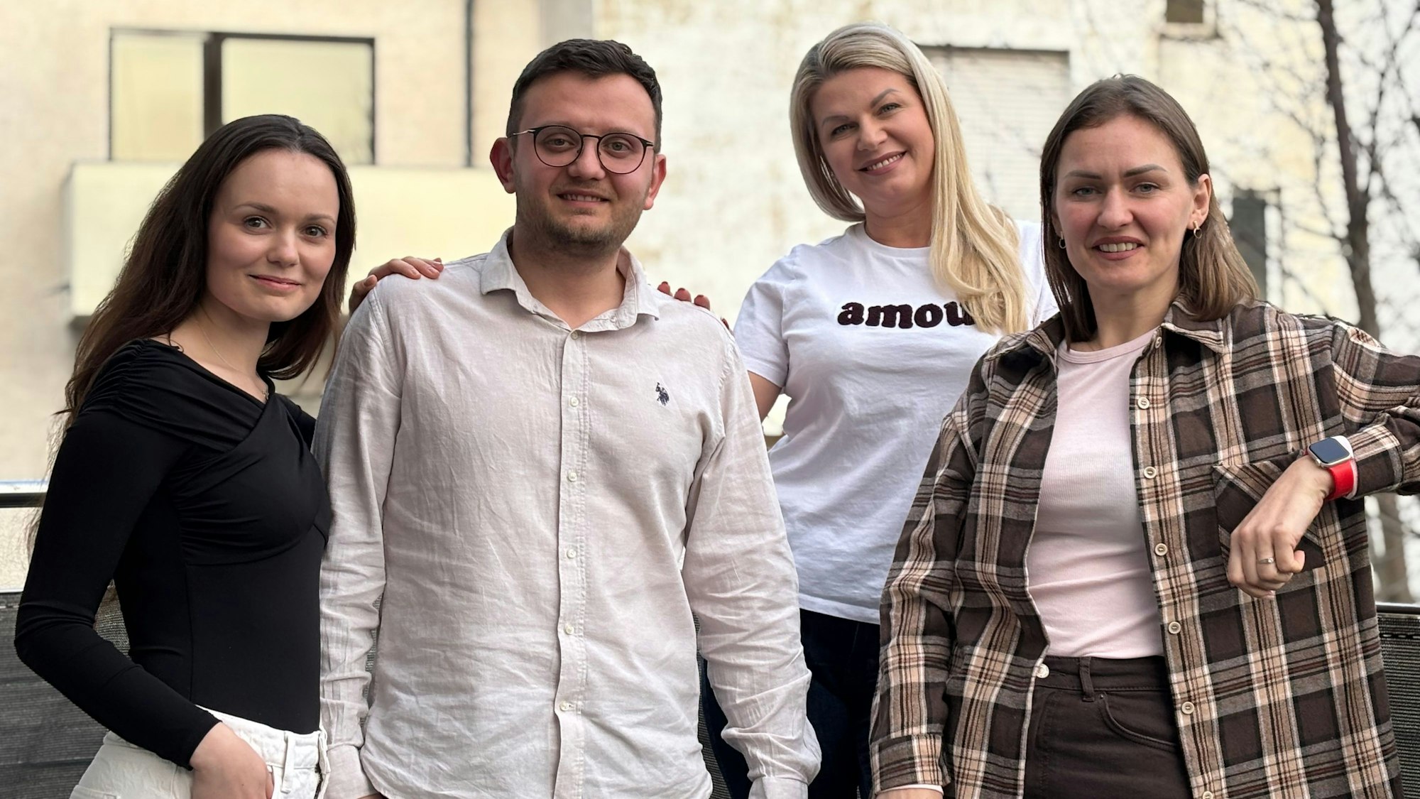 Die Obengenannten stehen zu viert auf einem Balkon und lächeln in die Kamera.