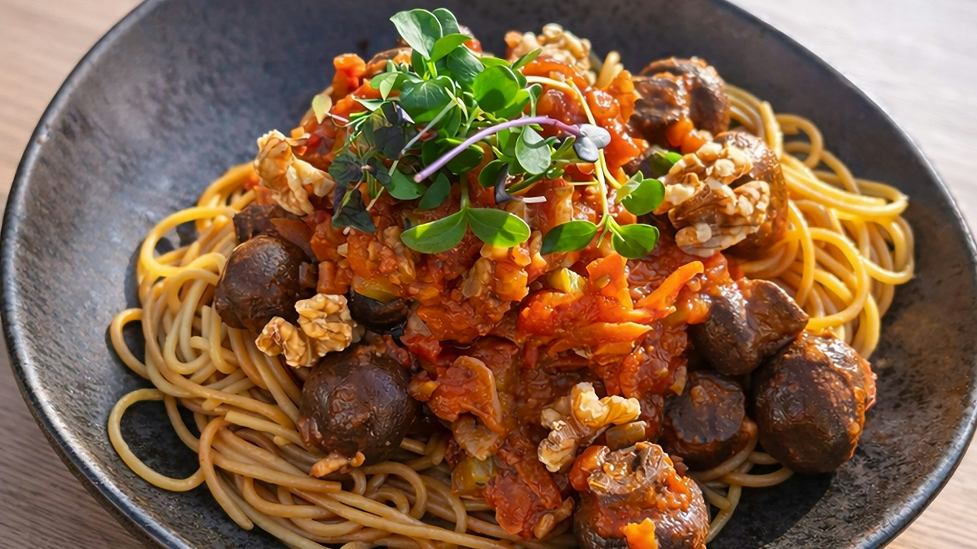 Spaghetti mit Walnuss-Pilz-Bolognese auf einem dunklen Teller.