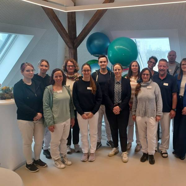 Eine Gruppe steht in einem Raum, in dem Physiotherapie stattfinden soll.