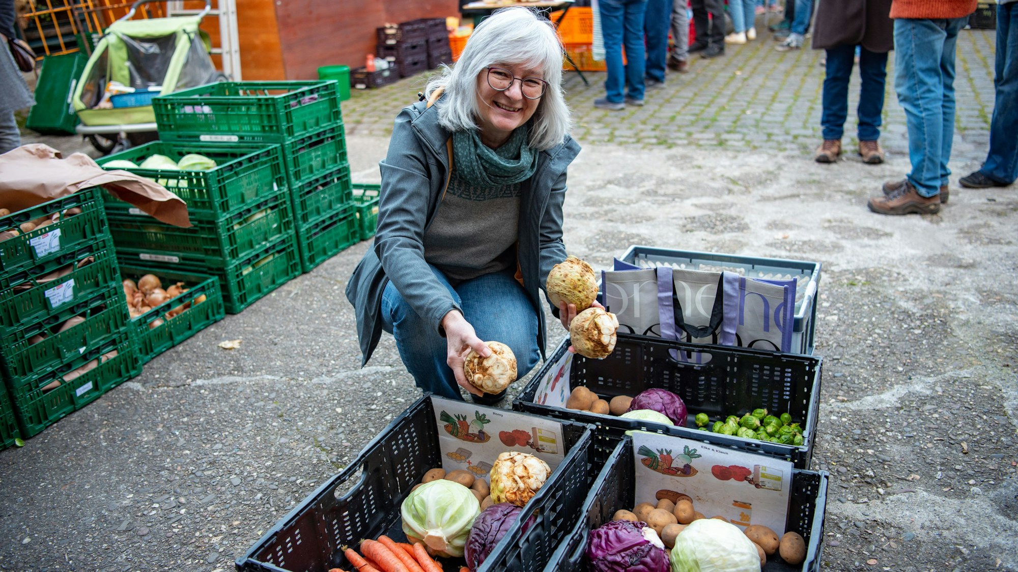 Aggi Peier kniet an Erntekisten und verteilt Sellerie.