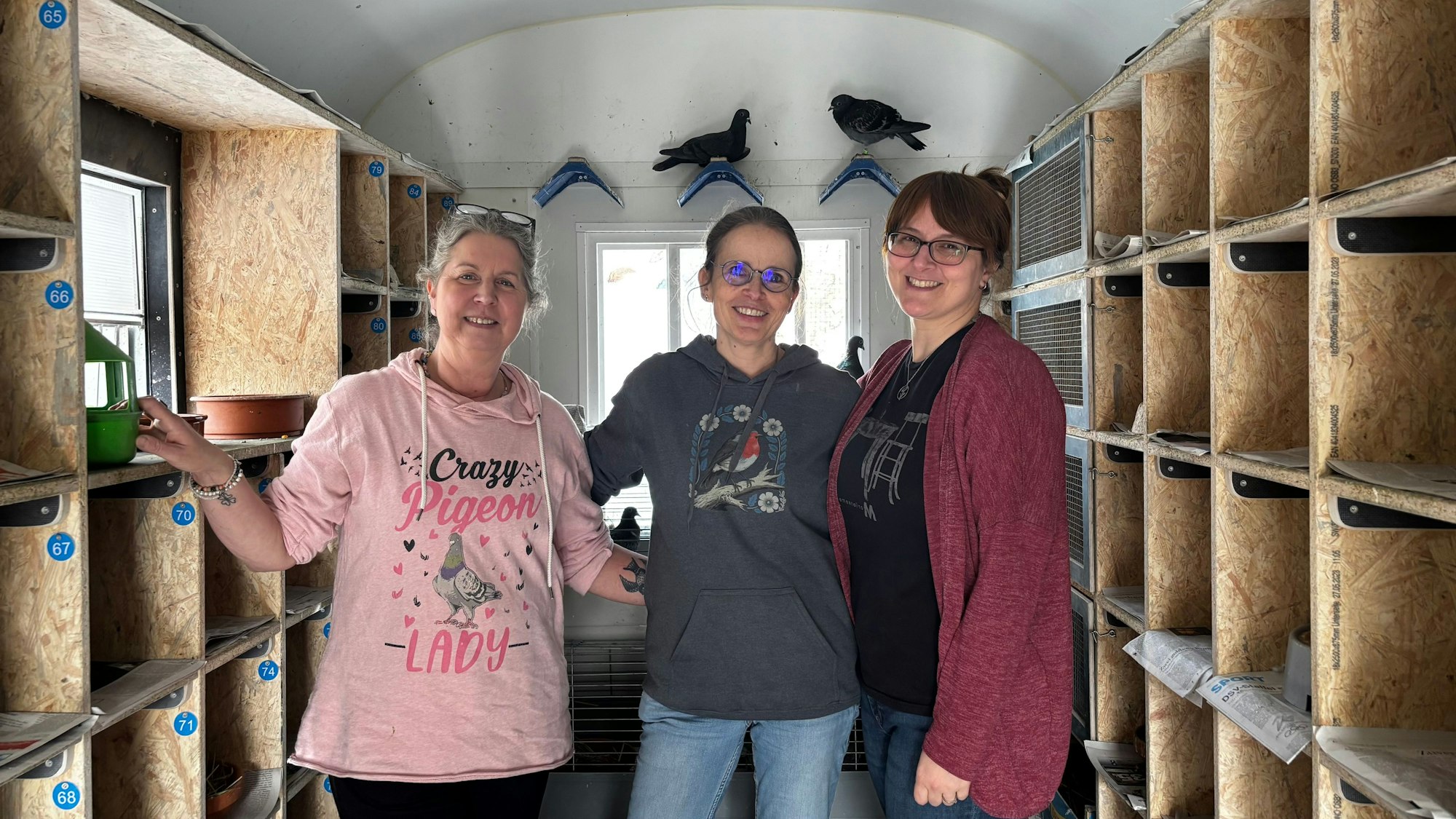 Drei Frauen blicken lächelnd in die Kamera. Im Hintergrund sitzen Tauben.