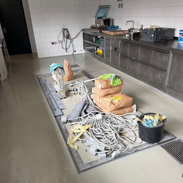 Eine gewerbliche Küche, auf dem Boden Kabel, Handwerkerflies, Säcke mit Baumaterialien, ein Eimer