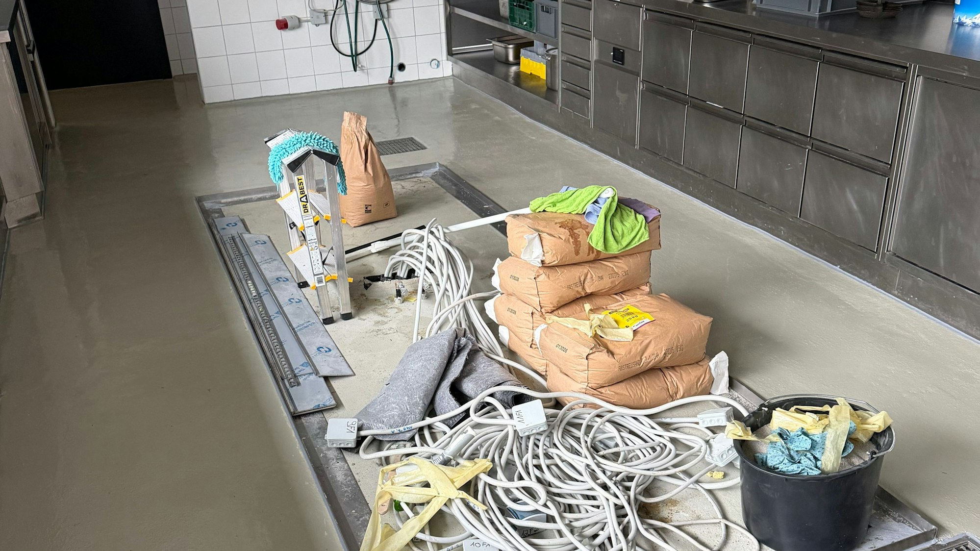 Eine gewerbliche Küche, auf dem Boden Kabel, Handwerkerflies, Säcke mit Baumaterialien, ein Eimer