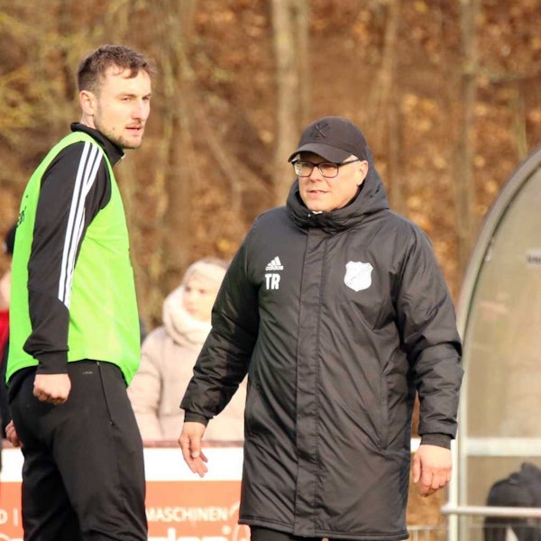 Marcel Timm trägt Kappe und dicke Jacke. Neben ihm macht sich ein Spieler warm.