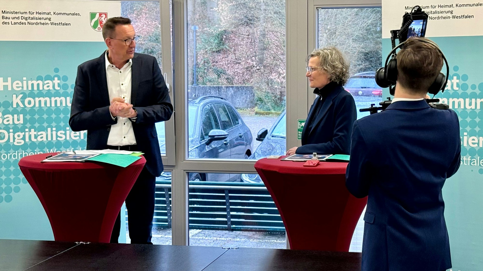 Dirk Runge und Ina Scharrenbach werden von einem Medienmitarbeiter des Ministeriums gefilmt.