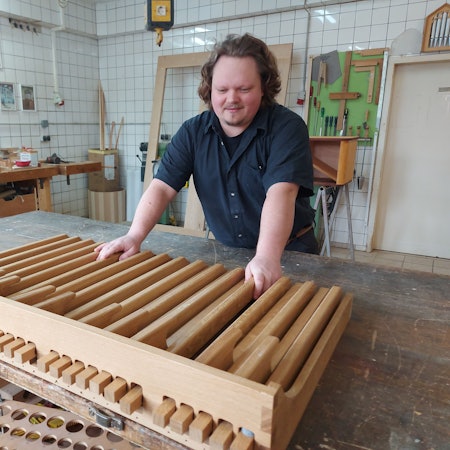 Ein Mann steht in einer Werkstatt an einem großen Lattenrost aus hellem Holz.