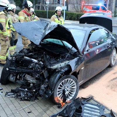 Feuerwehrleute stehen um ein schwer beschädigtes Auto in Bergisch Gladbach-Sand.