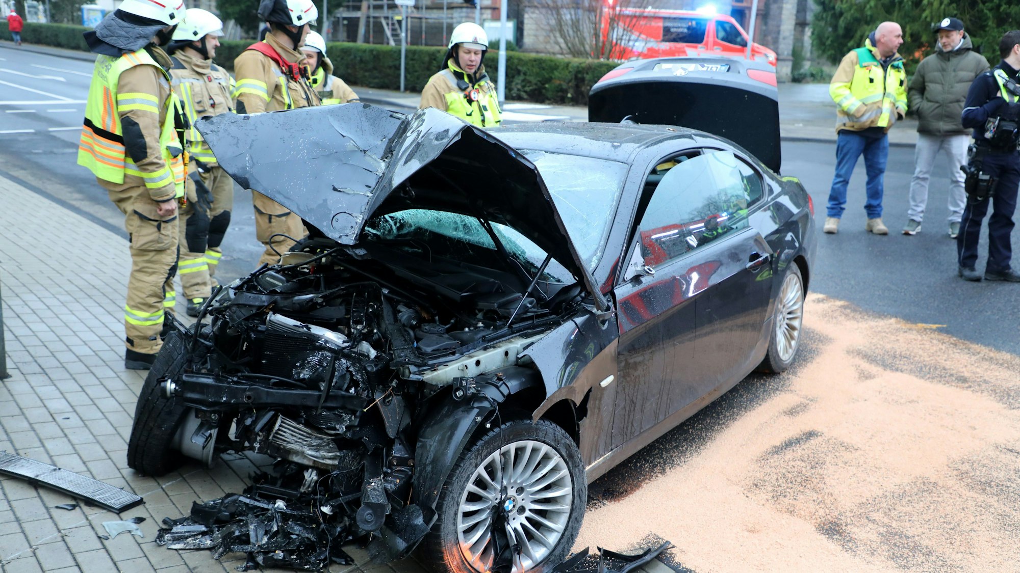Feuerwehrleute stehen um ein schwer beschädigtes Auto in Bergisch Gladbach-Sand.