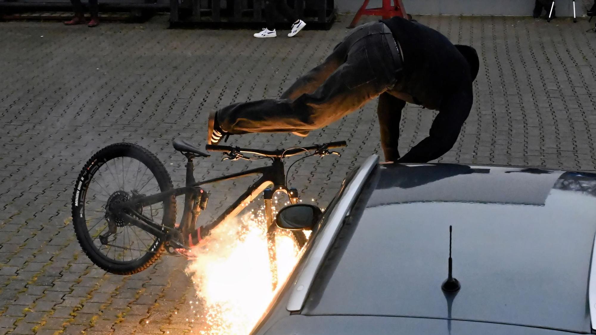 Ein Mann fällt mit seinem Fahrrad über ein Auto.