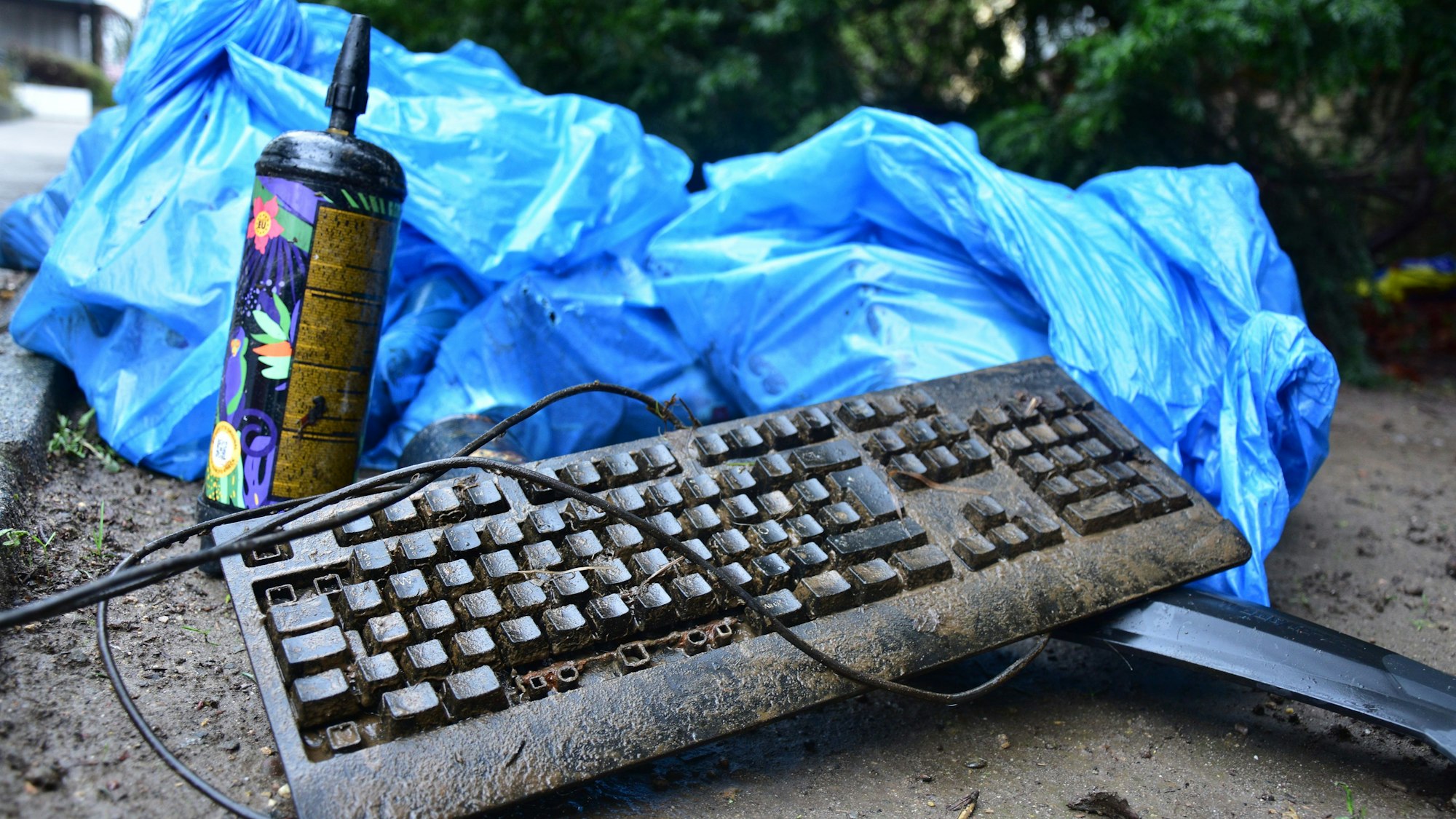 Eine dreckige Tastatur und eine Lachgas-Kartusche liegen vor einem blauen Müllbeutel.