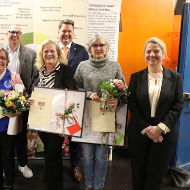 Eine Gruppe von Menschen, zum Teil halten sie Bilderrahmen und Urkunden in den Händen.