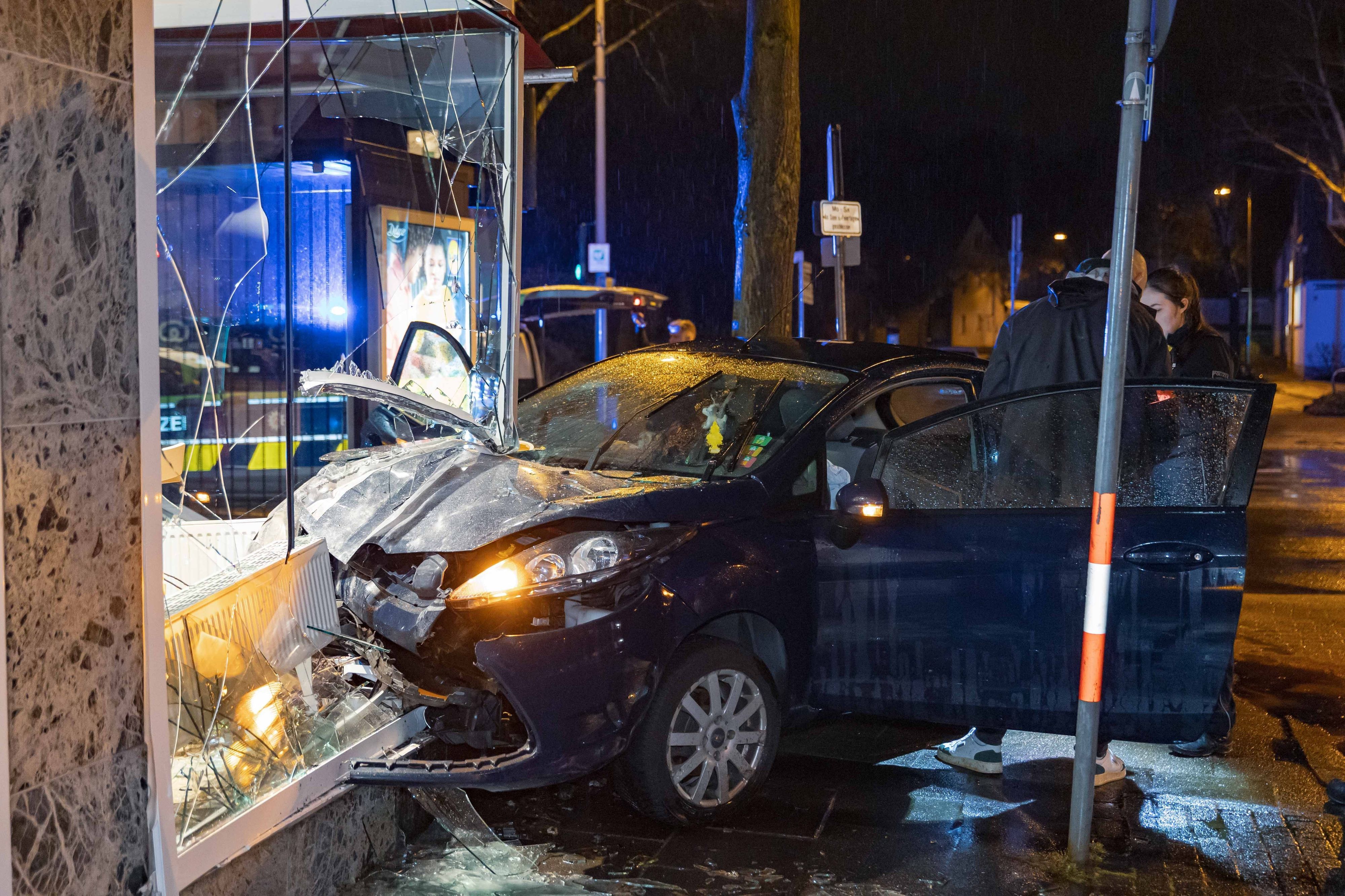 Ermittler stehen im März dieses Jahres an der Unfallstelle, wo ein Fahrer mit seinem Auto in das Schaufenster einer Leverkusener Bäckerei gekracht ist.