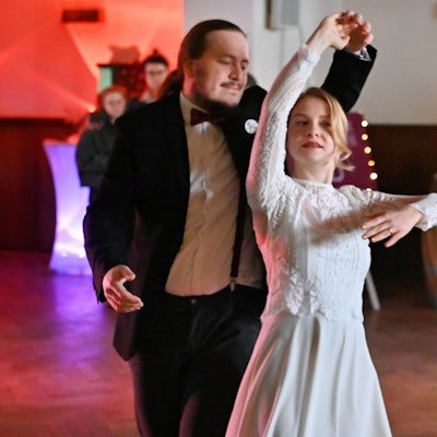 Eine Frau im Brautkleid und ein Mann im schwarzen Anzug tanzen zusammen.