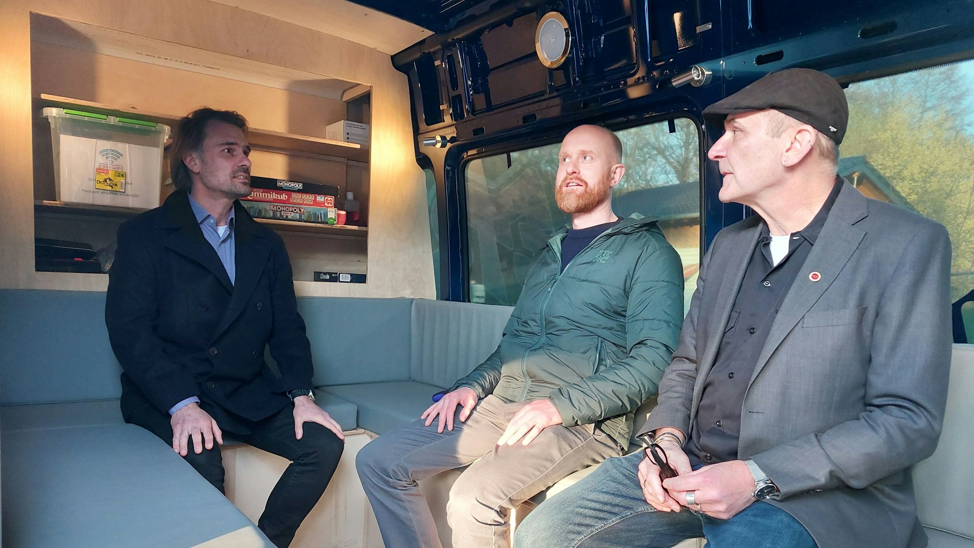 Drei Männer sitzen auf den Polstern im Jugendmobil und unterhalten sich.