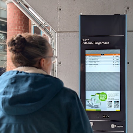 Das Foto zeigt eine Passantin vor der elektronischen Fahrplan-Stele am Rathaus.