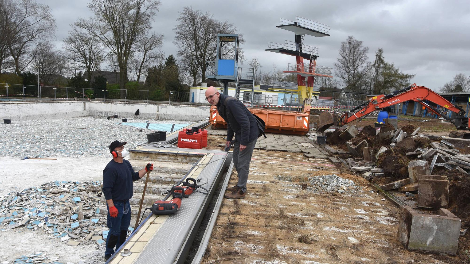 Das Foto zeigt Männer, die ein trockengelegtes Freibad sanieren.
