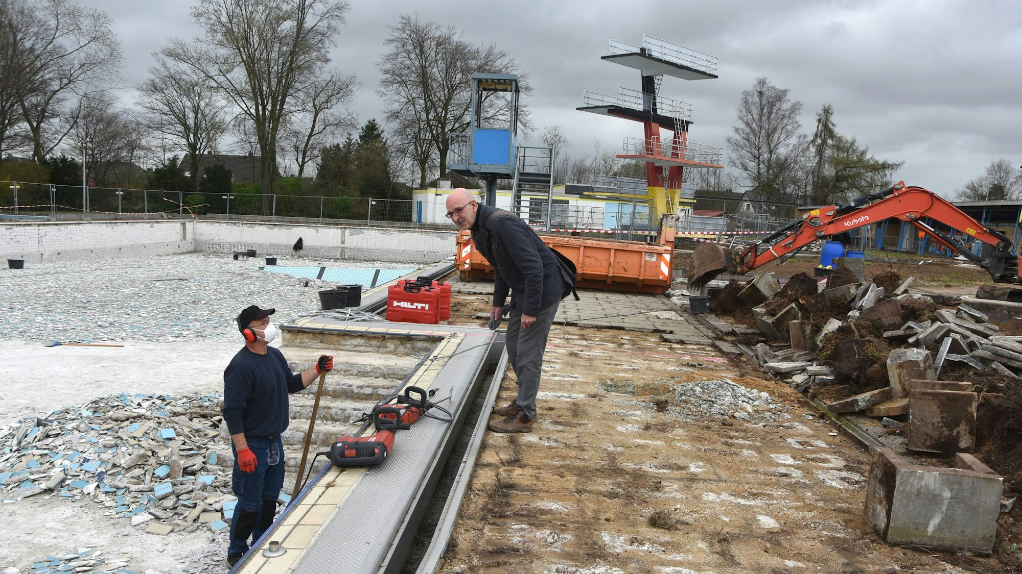 Das Foto zeigt Männer, die ein trockengelegtes Freibad sanieren.