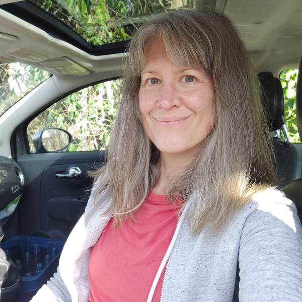 Auf dem Bild ist das Portrait einer Frau zu sehen, die am Steuer ihres Autos sitzt.