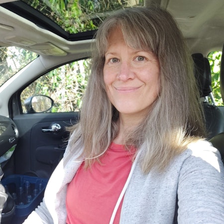 Auf dem Bild ist das Portrait einer Frau zu sehen, die am Steuer ihres Autos sitzt.