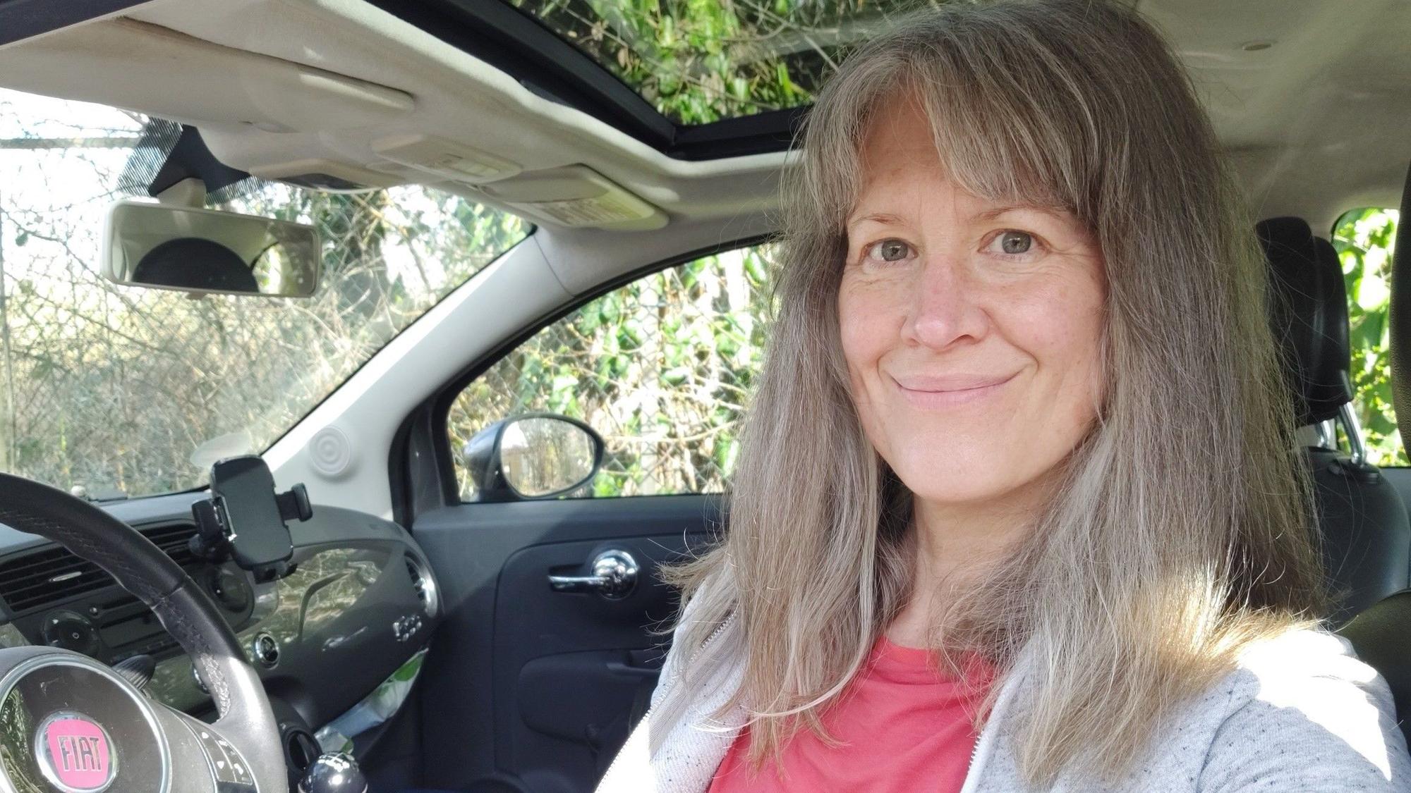Auf dem Bild ist das Portrait einer Frau zu sehen, die am Steuer ihres Autos sitzt.